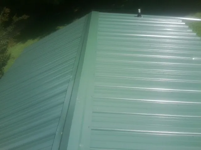 New green metal panels meeting at the ridge of a roof — Flat Roof Repair work by our crew in Keithville