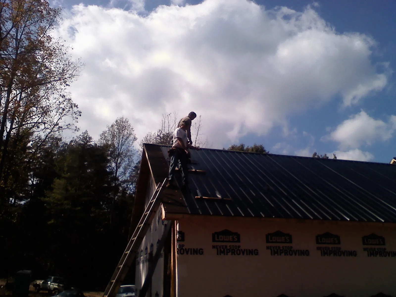 Roofer fastening dark metal panels high against a cloudy sky, from a Roof Inspection job in Keithville