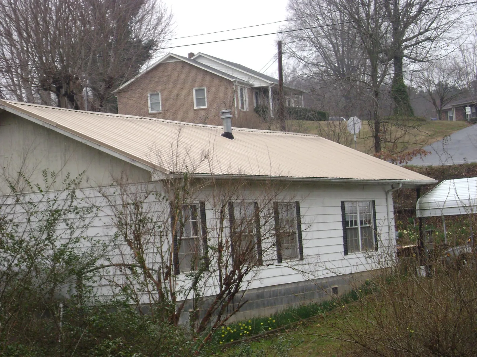 Tan metal roof on a white sided house set into a hillside — Commercial Roofing by Roofing Brothers in Keithville