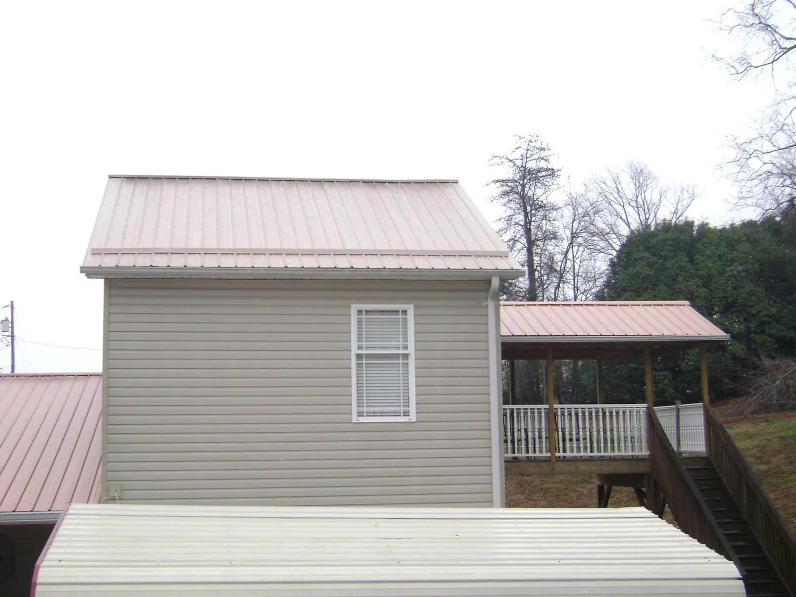 Tan metal roofs on a two story addition and attached porch, from a Roof Replacement job in Keithville